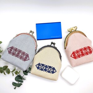May include: Three small coin purses with different colored fabric and embroidered designs. The purses are closed and have a metal clasp. The purses are on a white surface.