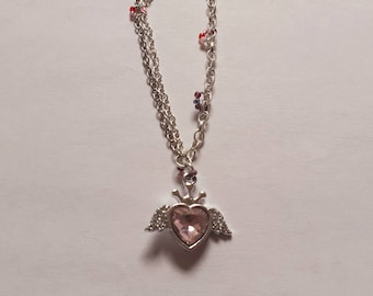 May include: A silver chain necklace with a pink heart pendant. The heart has wings and a crown on top.