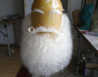 May include: A white wig with a long beard and mustache on a mannequin head. The head is made of a yellow material and has a plastic covering. The wig is styled with a mustache and beard.
