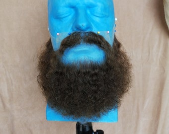 May include: A blue mannequin head with a long, brown, curly beard. The beard is attached to the mannequin with pins.