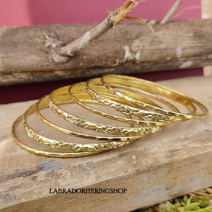 May include: A set of seven gold-toned bangles with a floral design. The bangles are stacked on top of each other and have a hammered texture.