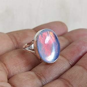 May include: A silver ring with a large oval-shaped iridescent opal gemstone. The opal has a blue, pink, and orange color.