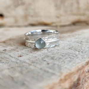 May include: A silver ring with a hammered band and a light blue gemstone. The ring is on a wooden surface.