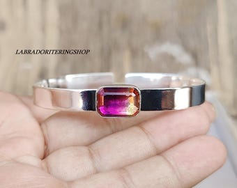May include: A silver bangle bracelet with a pink and orange gemstone set in the center.