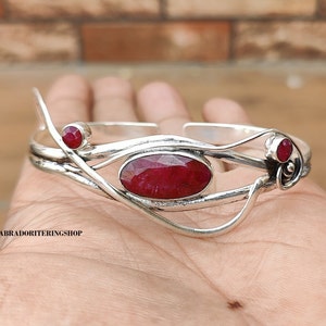 May include: Silver bangle bracelet featuring a red ruby gemstone set in a delicate, twisted design.