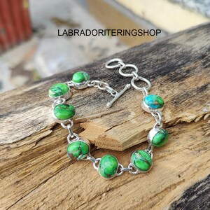 Könnte beinhalten: Ein silbernes Armband mit ovalen grünen und türkisfarbenen Edelsteinen. Die Steine sind in einem silbernen Rahmen gefasst und durch eine silberne Kette verbunden. Das Armband hat einen Knebelverschluss. Der Text "LABRADORITERINGSHOP" ist sichtbar.