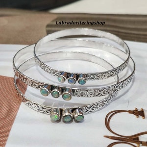Puede incluir: Conjunto de cuatro pulseras de plata con un diseño floral adornado y tres piedras de ópalo en cada pulsera.
