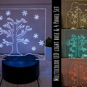 May include: A multicolor LED light base and four panel set with a tree design. The panels depict a tree in different seasons: winter, spring, summer, and fall. The base is black and has a button to change the color of the light.