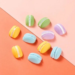 May include: A collection of colorful macarons in shades of yellow, green, blue, and purple, with white filling. The macarons are arranged on a two-tone pink and orange background. These sweet treats are a delightful confection.