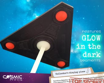 May include: Black triangular display piece with three red circles and a central white support. The text "GLOW in the dark" is visible. The display piece is a collector's item.