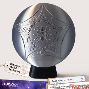 Puede incluir: Una esfera de metal plateado con un patrón grabado en forma de estrella, un diseño central similar a un circuito y detalles circulares. La esfera descansa sobre una base negra. Una etiqueta blanca sujeta por un cordel dice Display Stand Included.