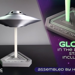 May include: A silver UFO model with a white stand and a grey base. The base has the text "S4 'Sports Model' 1989". The stand glows in the dark. The words "Glow in the Dark Stand Included" are also visible.