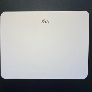May include: A white card with rounded corners and a monogram of the letters "JSA" in the center.
