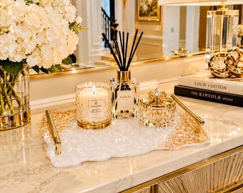 May include: A rectangular white and gold resin tray with gold metal handles, holding a Voluspa Blanc de Blancs candle, a Culti Milano reed diffuser with black reeds, and a small round crystal jar with a gold lid featuring a decorative finial.