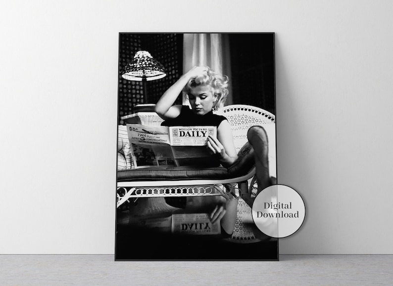 May include: Black and white framed print featuring a woman reading a newspaper with the headline "MOTION PICTURE DAILY." She is seated in a white wicker chair. A lamp with a patterned shade is visible in the background. The print is labeled "Digital Download."