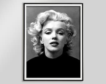 May include: Black and white framed portrait of Marilyn Monroe. The image features a close-up of her face, with her signature blonde curls and dark eyeliner. She is wearing a black top and looking directly at the viewer.