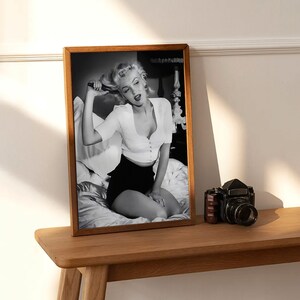 a black and white photo of a woman on a shelf next to a camera