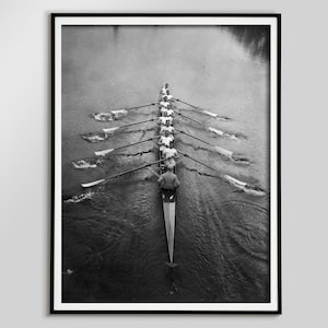 Puede incluir: Impresión enmarcada en blanco y negro de un equipo de remo en una embarcación larga sobre el agua. Se ven ocho remeros con camisas blancas y un timonel. Los remos crean un patrón simétrico.