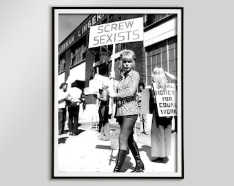 May include: Black and white framed photograph of a protest. A woman holds a sign that reads "SCREW SEXISTS". Other protesters hold signs with text. The image is in black and white.