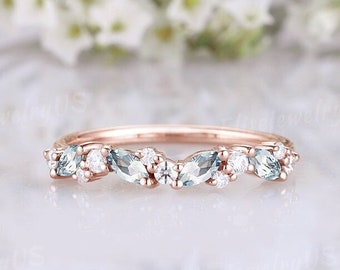 May include: A delicate rose gold band with a row of marquise and round cut aquamarine and white gemstones.