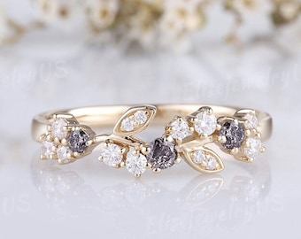 May include: A delicate gold band ring with a floral design featuring small white and black diamonds. The ring is set on a white background.
