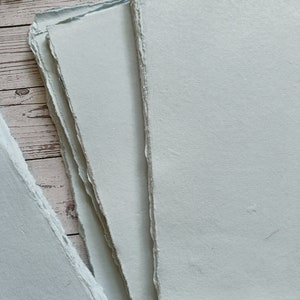 May include: Stack of light blue handmade paper sheets with deckled edges.