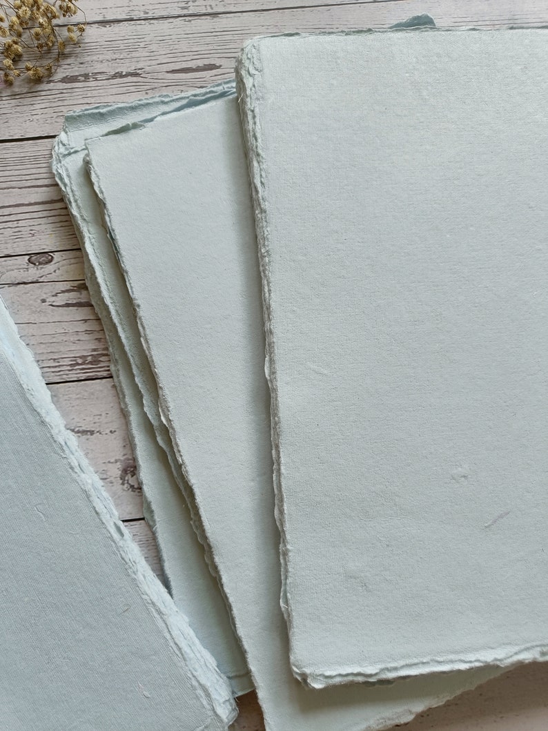 May include: Stack of light blue handmade paper sheets with deckled edges.
