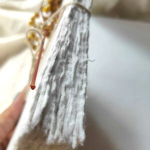 May include: A stack of handmade, textured white paper, bound with twine and adorned with dried yellow flowers. The paper has a rough, uneven surface, suggesting a natural, artisanal quality. The overall aesthetic is rustic and organic.