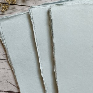 May include: Three sheets of light blue handmade paper with deckled edges.