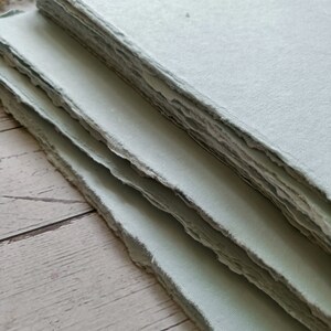 May include: A stack of light blue handmade paper with deckled edges. The paper is textured and has a slightly rough surface.
