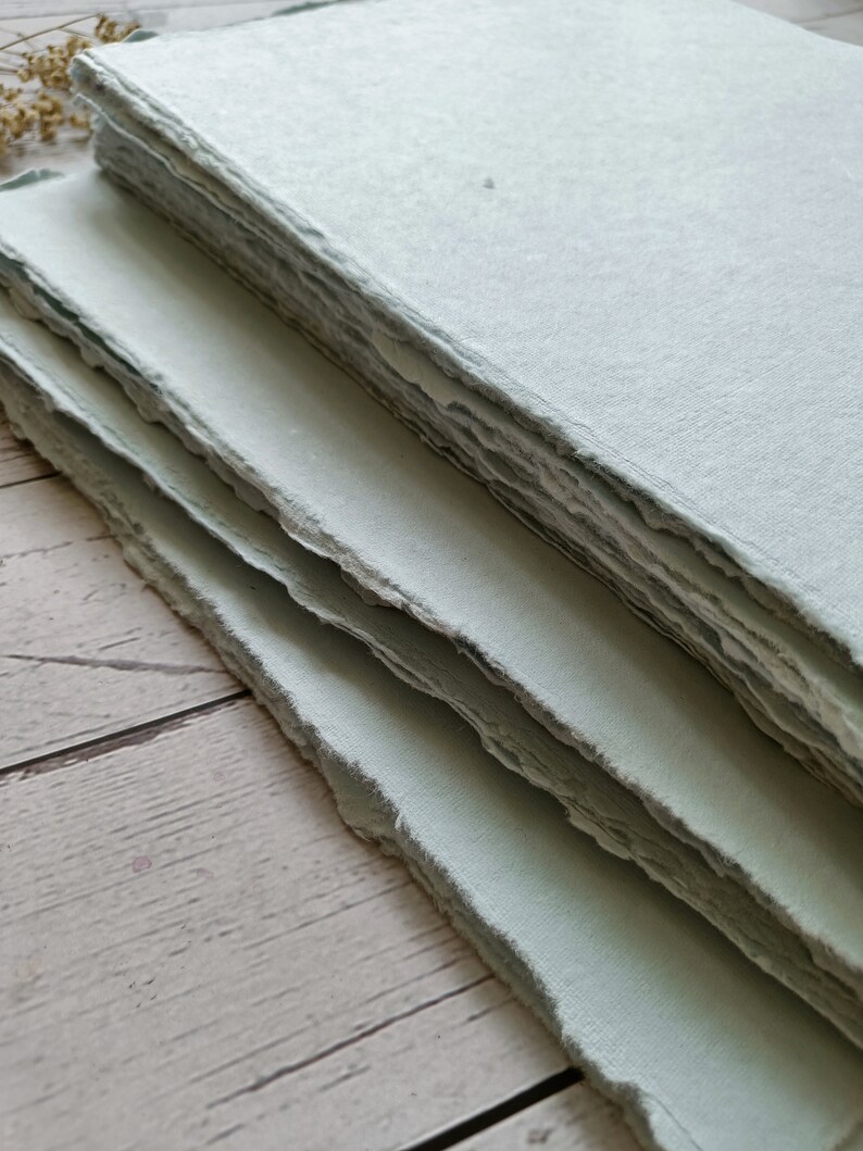 May include: A stack of light blue handmade paper with deckled edges. The paper is textured and has a slightly rough surface.