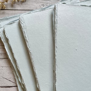 May include: Stack of four light blue handmade paper sheets with deckled edges.