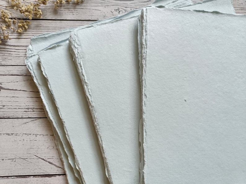 May include: Stack of four light blue handmade paper sheets with deckled edges.
