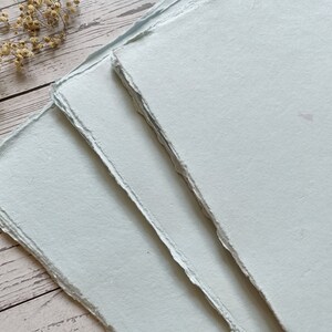 May include: Three sheets of light blue handmade paper with deckled edges.