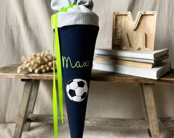 May include: A blue and white school cone with a soccer ball design and the name "Max" embroidered on it. The cone is tied with a bright green ribbon.