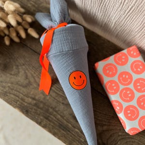 Sac Kita / sac pour frères et sœurs en mousseline gris-bleu avec broderie sourire en orange fluo et ruban en orange fluo