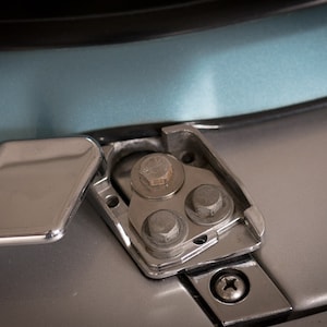 May include: Close-up of a chrome-plated car door latch with a silver screw and three nuts. The latch is open and the door handle is visible.