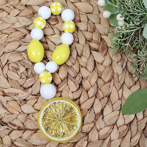May include: A yellow and white beaded garland with a lemon slice charm. The beads are made of wood and have a checkered pattern.