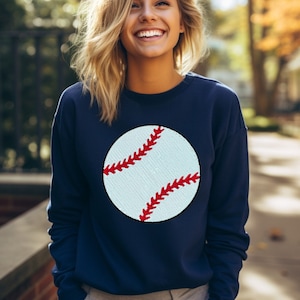 May include: A navy blue sweatshirt with a white baseball graphic featuring red stitching.