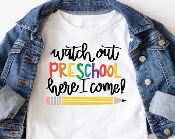 Puede incluir: Camiseta blanca con el texto "watch out PRESCHOOL here I come!" en colores arcoíris con un lápiz amarillo debajo.