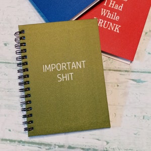 May include: A green spiral bound notebook with the text "IMPORTANT SHIT" printed in white on the front cover.