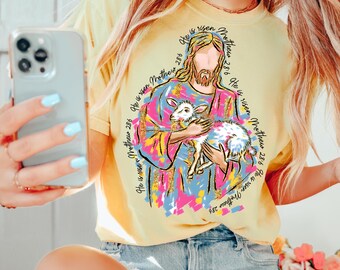 May include: A yellow t-shirt with a colorful graphic of Jesus holding a lamb. The graphic is surrounded by the text "He is risen Matthew 28:6" repeated multiple times.