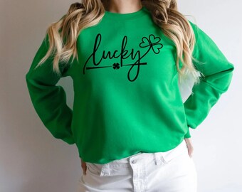 May include: A bright green sweatshirt with the word "lucky" in a cursive font, accompanied by a small shamrock graphic. The sweatshirt is a solid color, and the text and graphic are in black.
