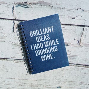 May include: A blue spiral bound notebook with the text "BRILLIANT IDEAS I HAD WHILE DRINKING WINE." printed in white.