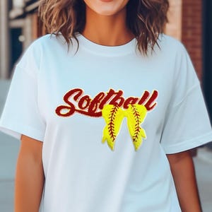 May include: White t-shirt with a red "Softball" graphic and a yellow softball with red stitching in a bow shape.