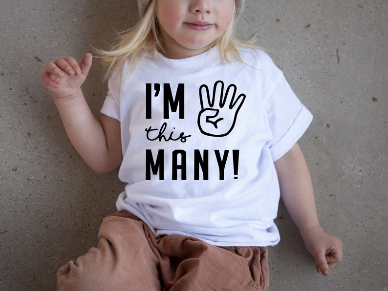 Może przedstawiać: Biała koszulka z czarnym napisem "I'm this many!" i czarną ręką z uniesionymi czterema palcami.
