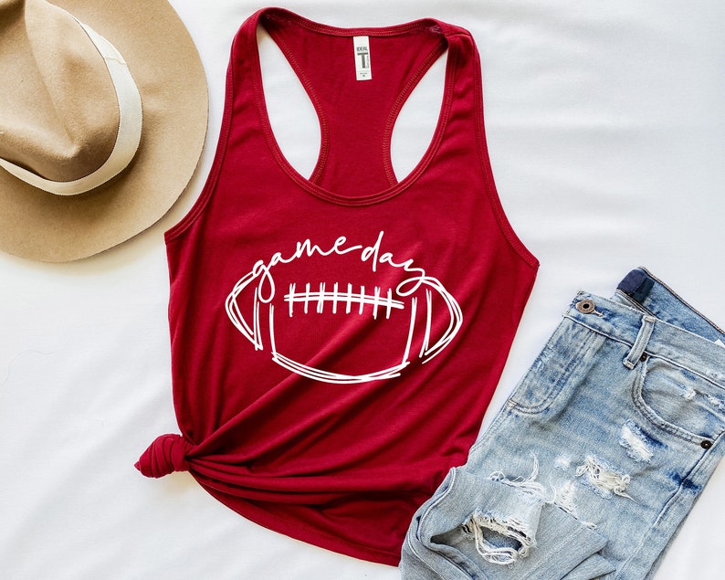 May include: A red tank top with a white graphic of a football and the text "game day".