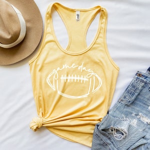 May include: A yellow tank top with a white outline of a football and the text "game day".