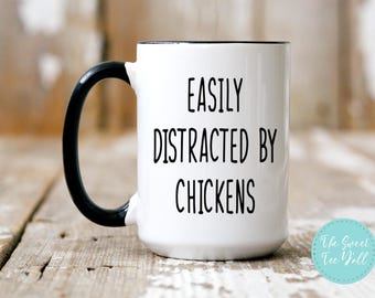 May include: White ceramic coffee mug with a black handle and black rim. The mug has the text "EASILY DISTRACTED BY CHICKENS" printed in black on the front.