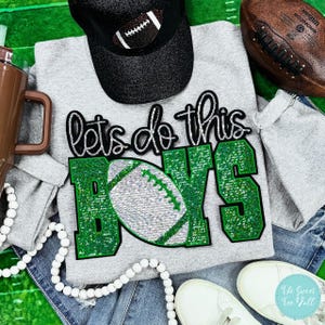 May include: Grey sweatshirt with the text "Let's do this Boys" in green glitter letters. A football is included in the design.